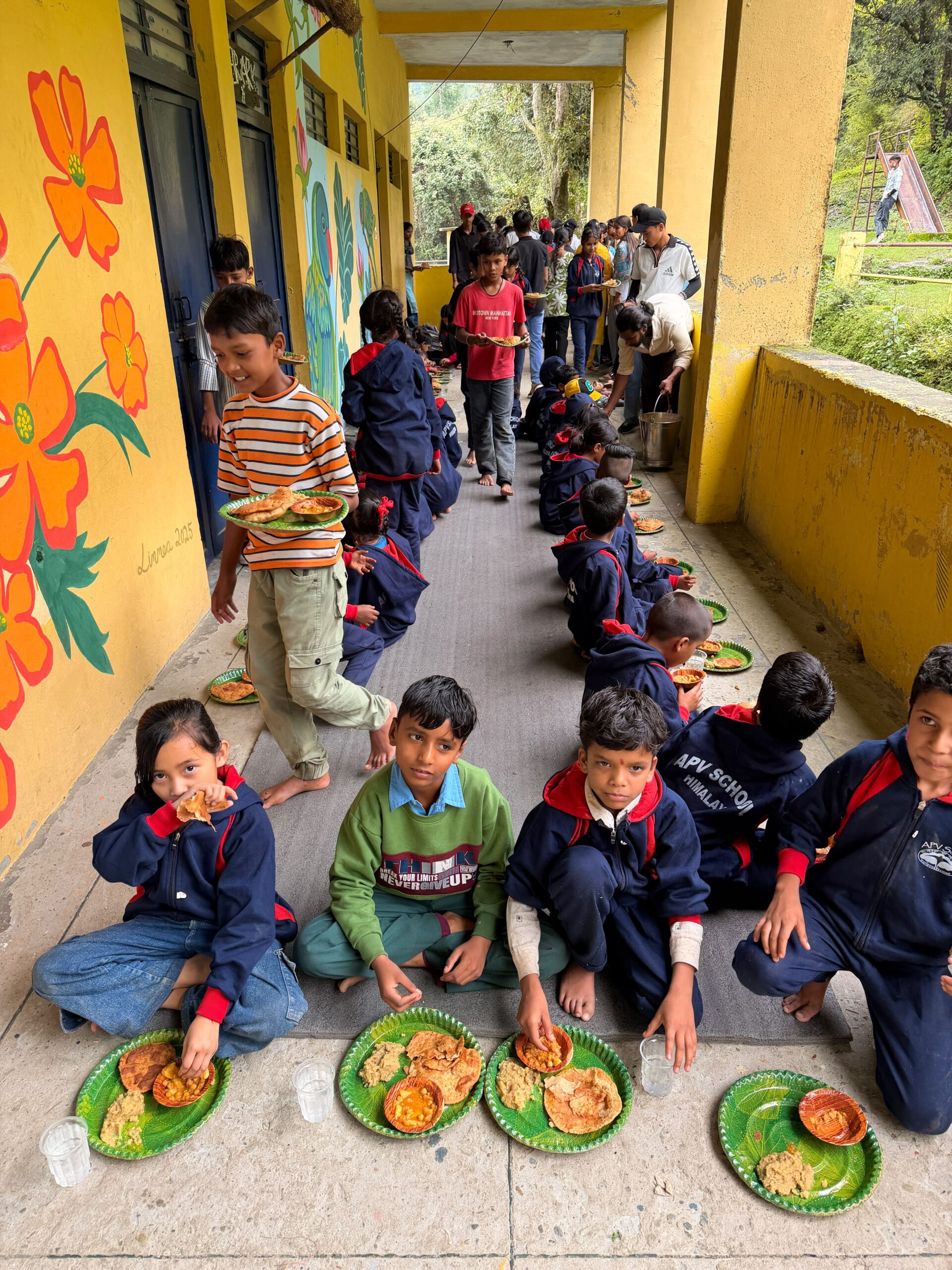 Children eating together in two long rows along the school veranda