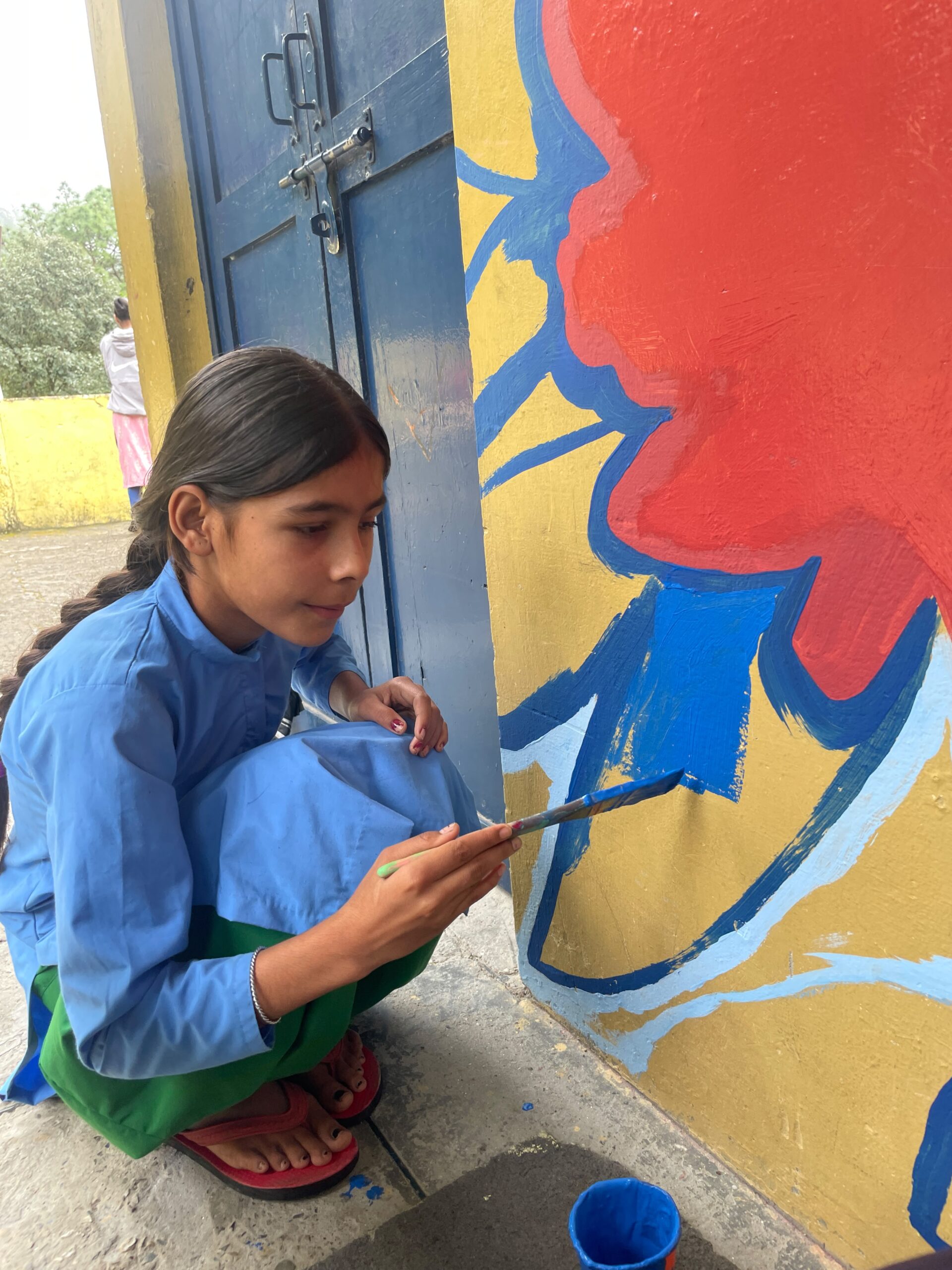 A student painting a mural on the school wall