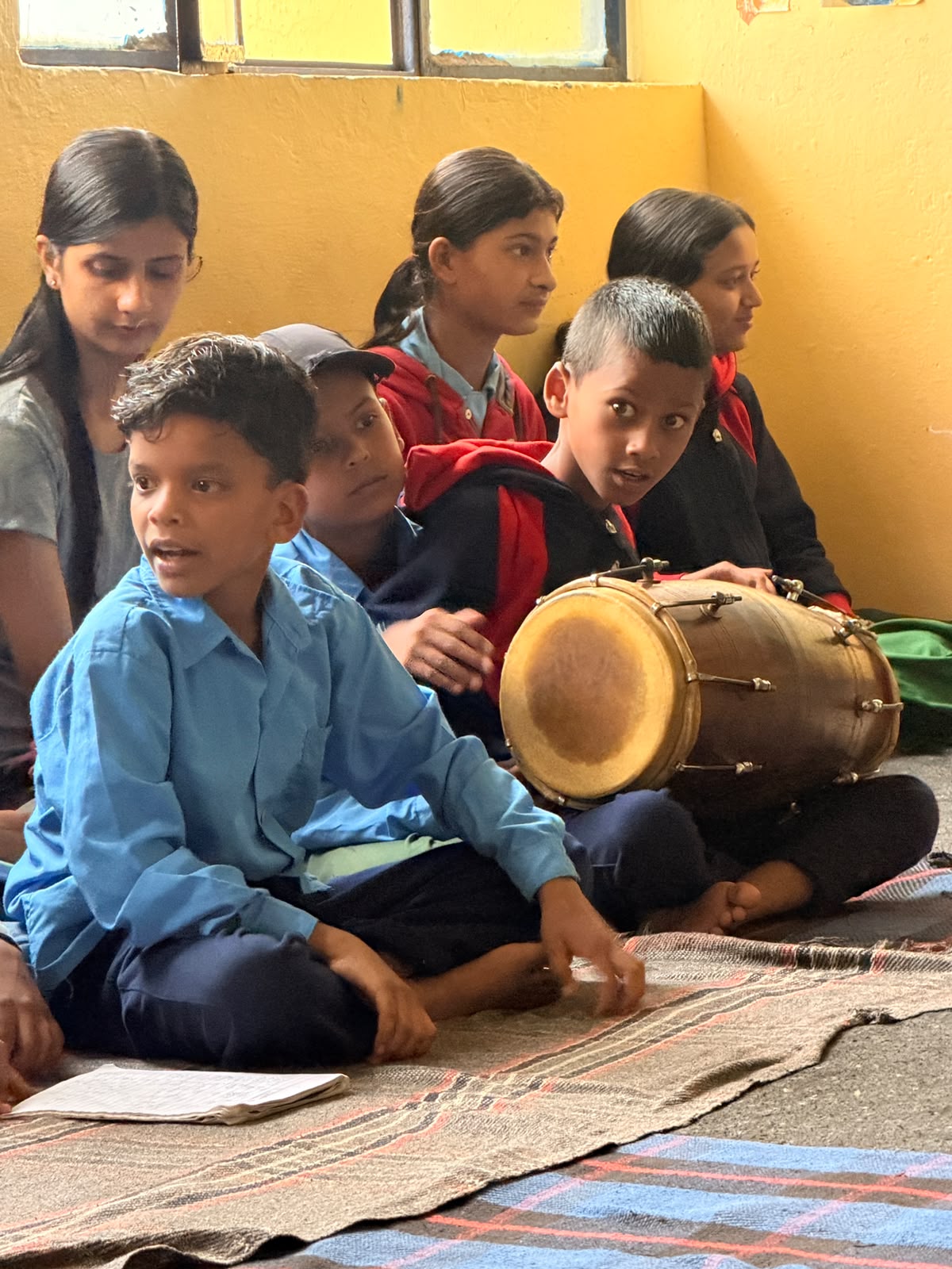 A student playing the madal while classmates gather round